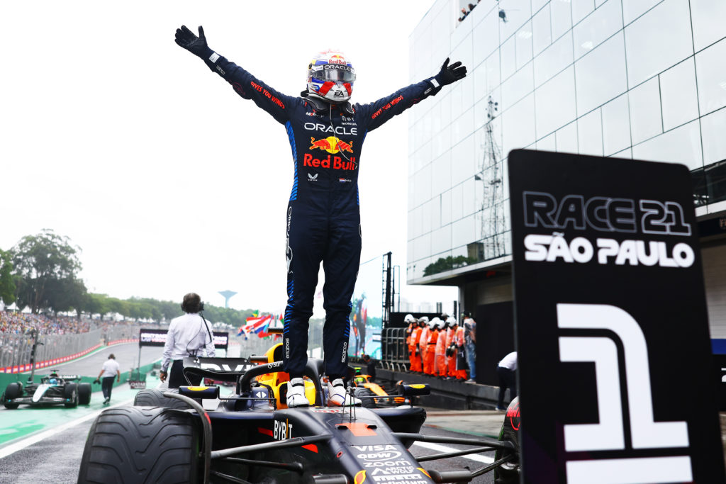 Max Verstappen celebrating his win at the 2024 Brazilian Grand Prix by standing on top of his Red Bull F1 car.