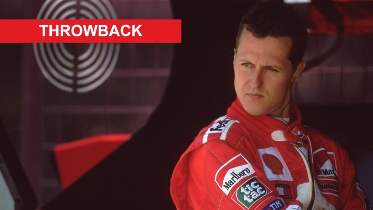 Michael Schumacher wearing a red Ferrari racing suit, sitting in the team garage with a focused expression. A red “THROWBACK” banner appears in the...