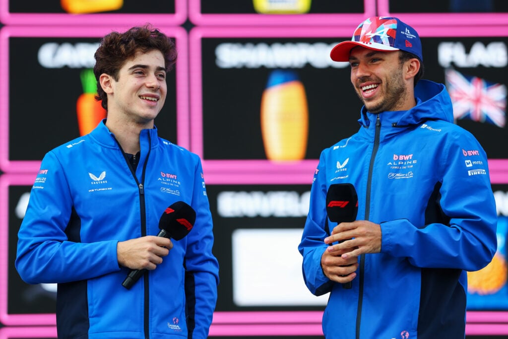 Franco Colapint and Pierre Gasly in Alpine blue jackets smiling whilst holding F1 branded microphones