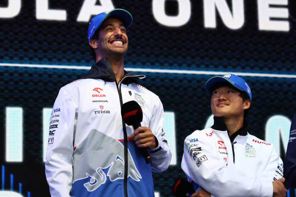 Yuki Tsunoda looking up at Daniel Ricciardo holding a microphone on stage at the 2024 Formula 1 Belgian Grand Prix