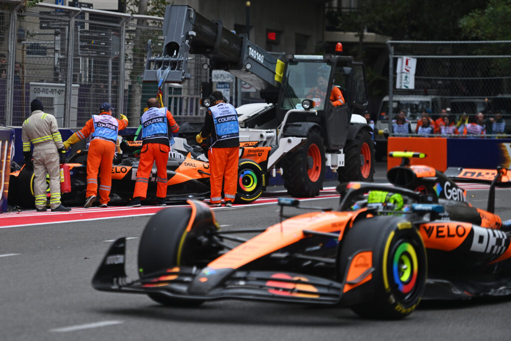 Lando Norris drives past several track marshals who are retreiving Oscar Piastri's crashed McLaren in the 2025 F1 Azerbaijan Grand Prix