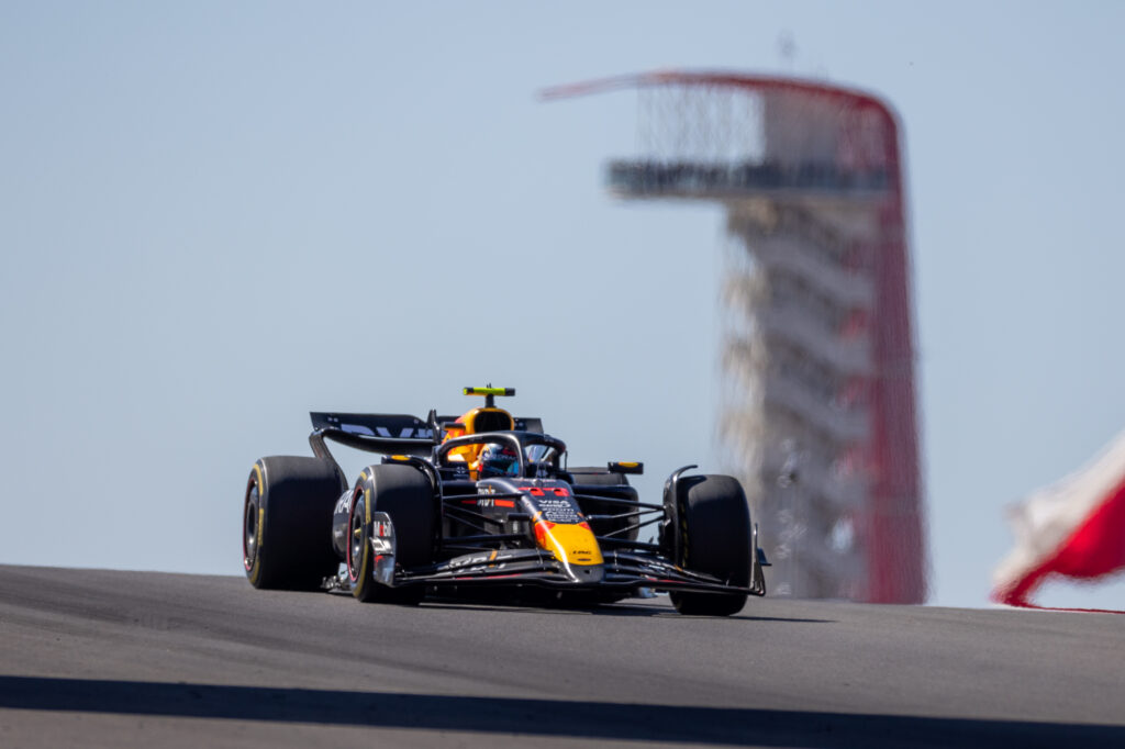 Sergio Perez's Red Bull banks over a hill at the Circuit of the Americas with the track's iconic tower in the background