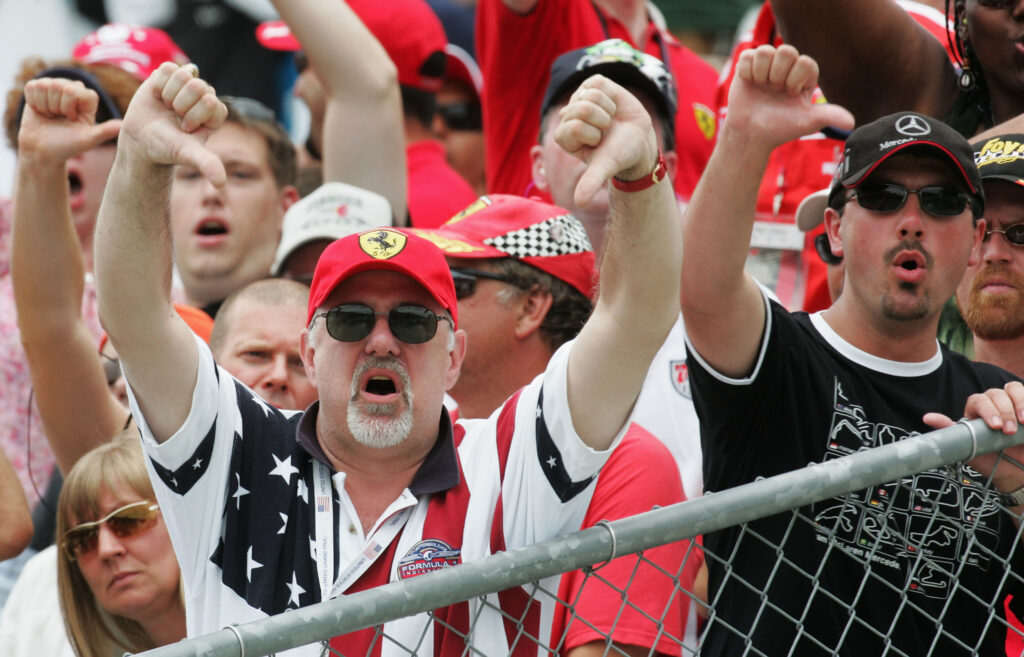 Fans in the stands of the 2005 United States Grand Prix sharing their frustration with thumbs down gestures at the camera.
