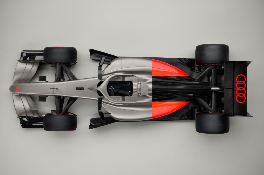 Birds eye view of the Audi R26 F1 car, with a silver front half and a black and red design on the back, with the Audi logo in red on the rear wing and nose tip