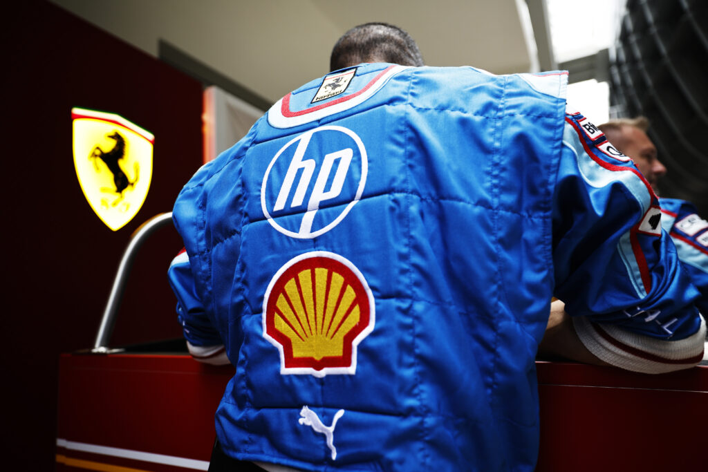 A Ferrari engineer with his back to the camera, which shows the HP and Shell logos on the back of their overalls.