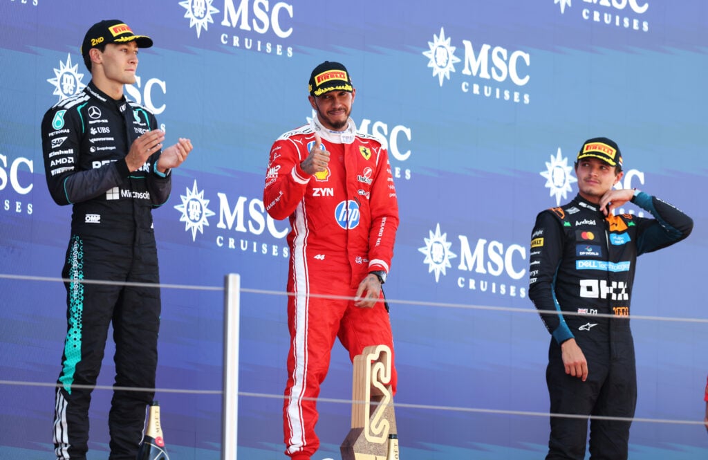 McLaren driver Lando Norris looks on as Ferrari's Lewis Hamilton celebrates winning the 2026 F1 Barcelona-Catalunya Grand Prix on the podium