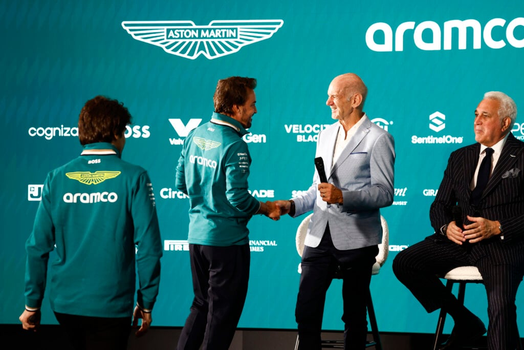 Aston Martin driver Fernando Alonso shakes hands with team principal Adrian Newey while owner Lawrence Stroll looks on.
